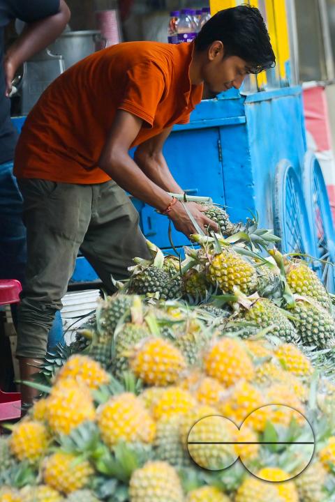 A city dweller purchases pineapple, a renowned summer fruit of Tripura, from a vendor's stall at a bustling roadside fruit market in Agartala