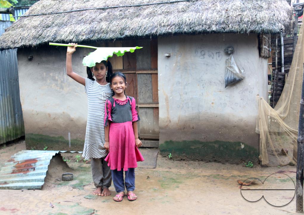 Rural Bangladeshi children happily posing for a photograph while covering their heads with a big leaf to prevent the sun