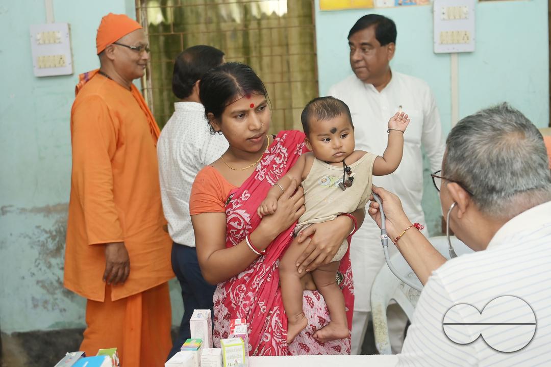 A doctor examining a boy during a visit by Swami Shubhakarananda (Maharaj) - Secretary of Ramakrishna Mission, along with Mayor Deepak Majumdar, the District Magistrate, and other officials inspect a health camp for flood victims at a temporary relief ca