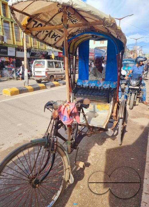 A rickshaw driver is framed in the rear window of the adjoining rickshaw, at the local market, in Agartala