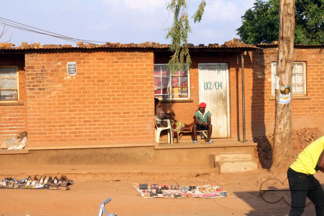 A woman and man are seated outside their home where she has set up a market in the yard at Dzaleka refugee camp in Dowa District, Malawi.
