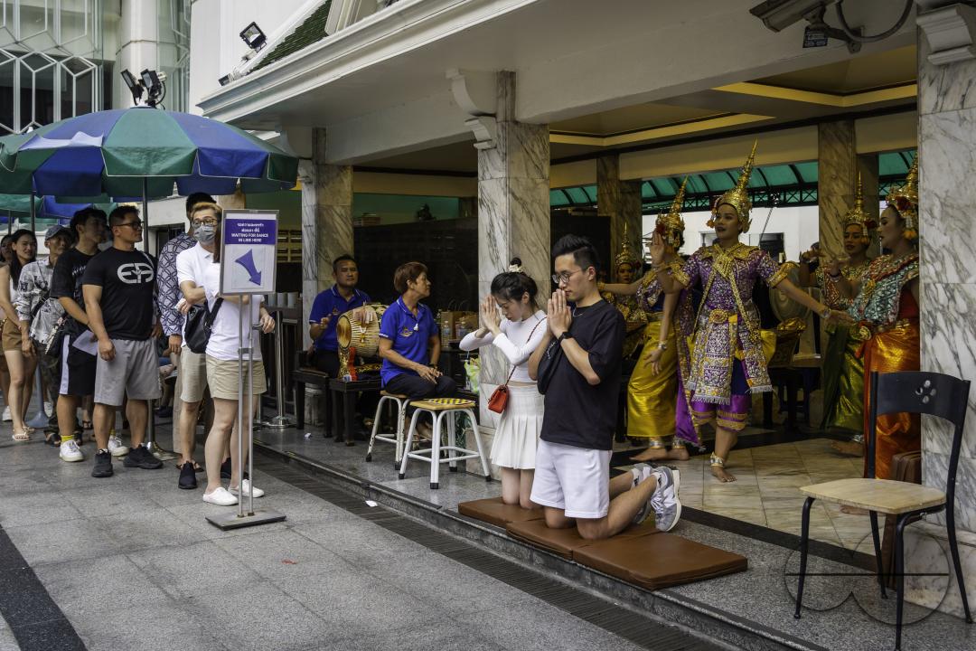 In the heart of downtown Bangkok, an Asian woman engages in prayer with in her hands an offering basket, at the Erawan Shrine