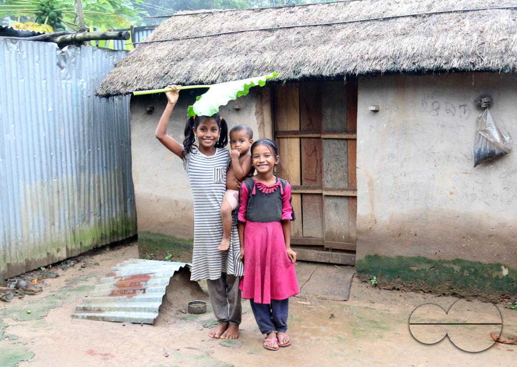 Rural Bangladeshi children happily posing for a photograph while covering their heads with a big leaf to prevent the sun