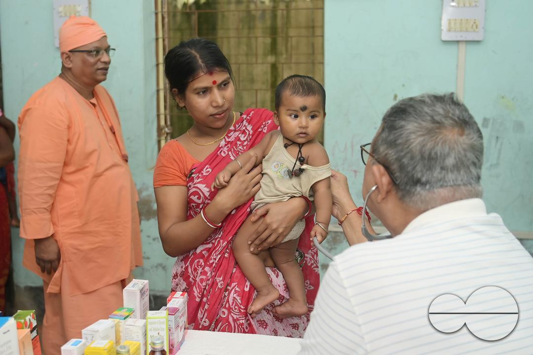 A doctor examining a boy during a visit by Swami Shubhakarananda (Maharaj) - Secretary of Ramakrishna Mission, along with Mayor Deepak Majumdar, the District Magistrate, and other officials inspect a health camp for flood victims at a temporary relief ca