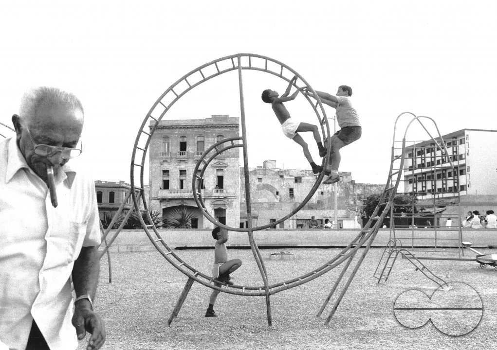 CUBA.ELDERLY MAN WITH CIGAR LOOKING AFTER HIS GRANDCHILDREN PLAYING IN A PARK IN HAVANA.1991