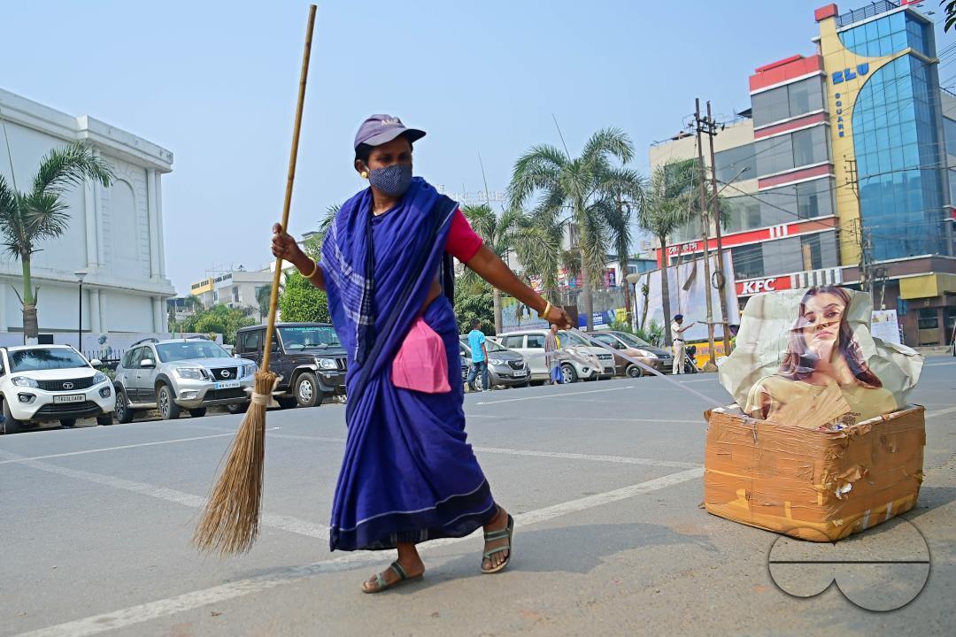 An employee of the municipality pulls a garbage collection box while sweeping and collecting garbage into it in Agartala