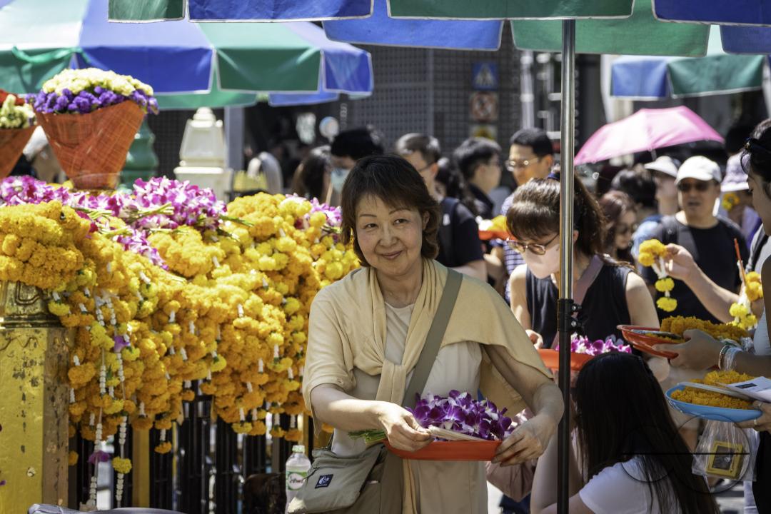 An elderly Asian woman is carrying a basket of offerings, at the Erawan Shrine, in downtown Bangkok