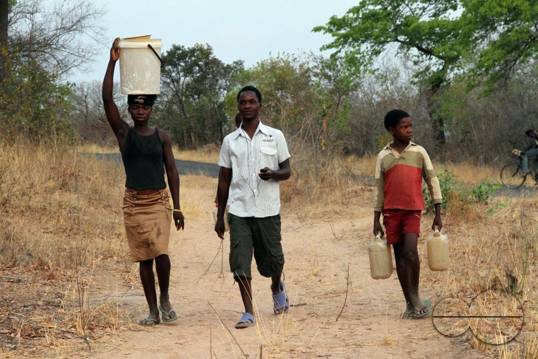 Young people are seen carrying containers full of water from a nearby river in Binga District
