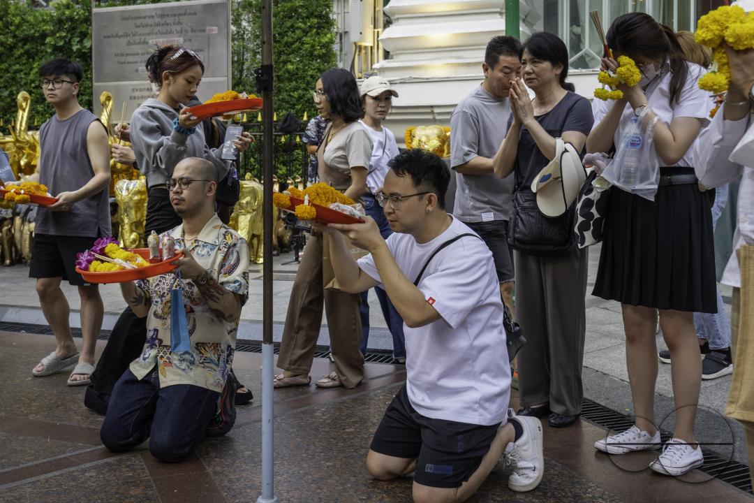 At the Erawan Shrine in downtown Bangkok, an Asian is praying with an offering basket in hand among the crowd
