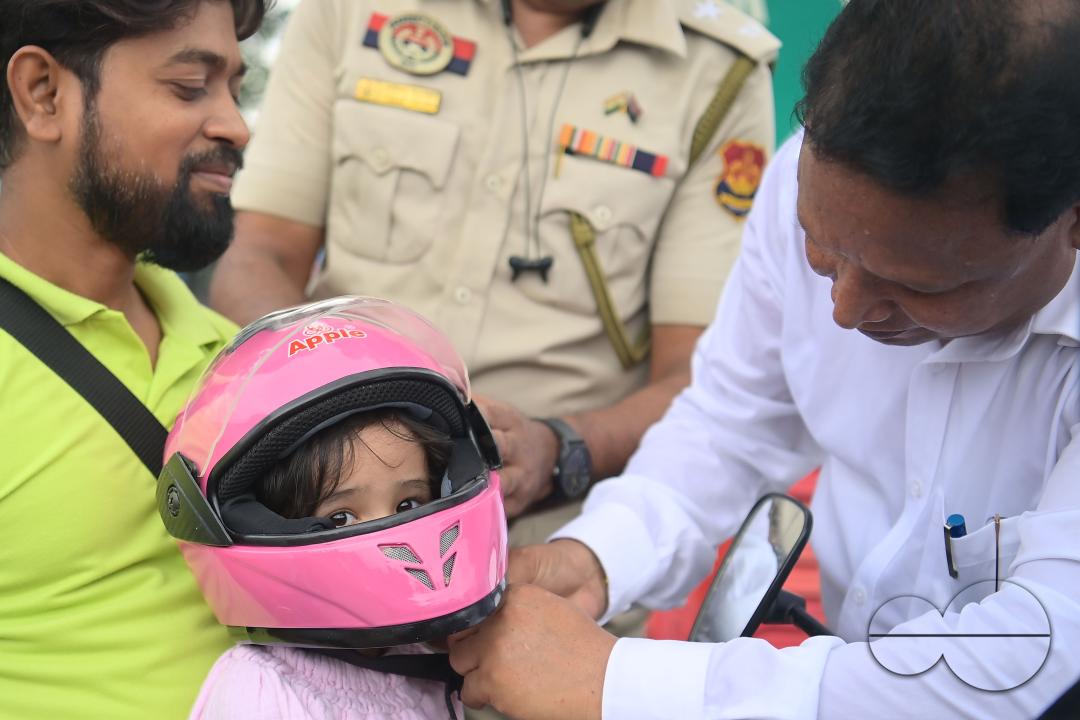 A traffic official puts a helmet on a kid who is riding on a motorcycle with her father during a helmet distribution program and a road safety awareness campaign organised by the Tripura Transport Department at Agartala