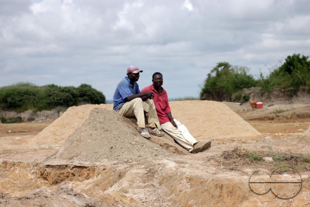 Two men are sitting on top of a mound of sand as they rest from digging for sand