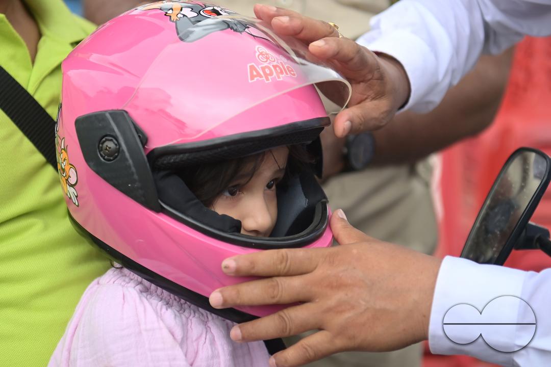 A traffic official puts a helmet on a kid who is riding on a motorcycle with her father during a helmet distribution program and a road safety awareness campaign organised by the Tripura Transport Department at Agartala