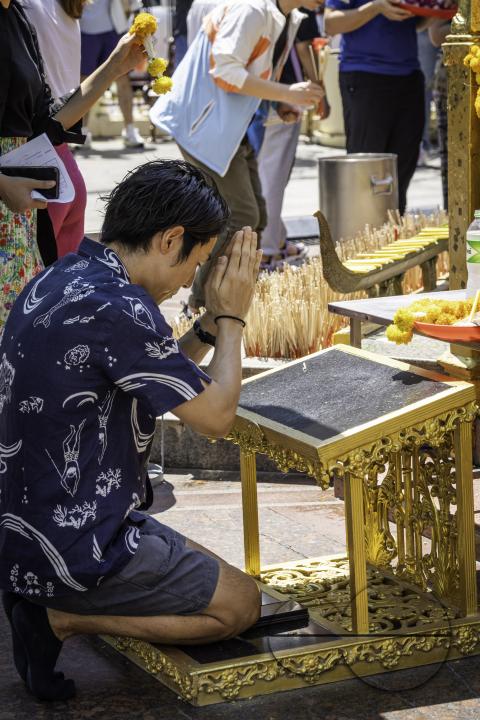 An Asian man is praying at the iconic Erawan Shrine, nestled in downtown Bangkok