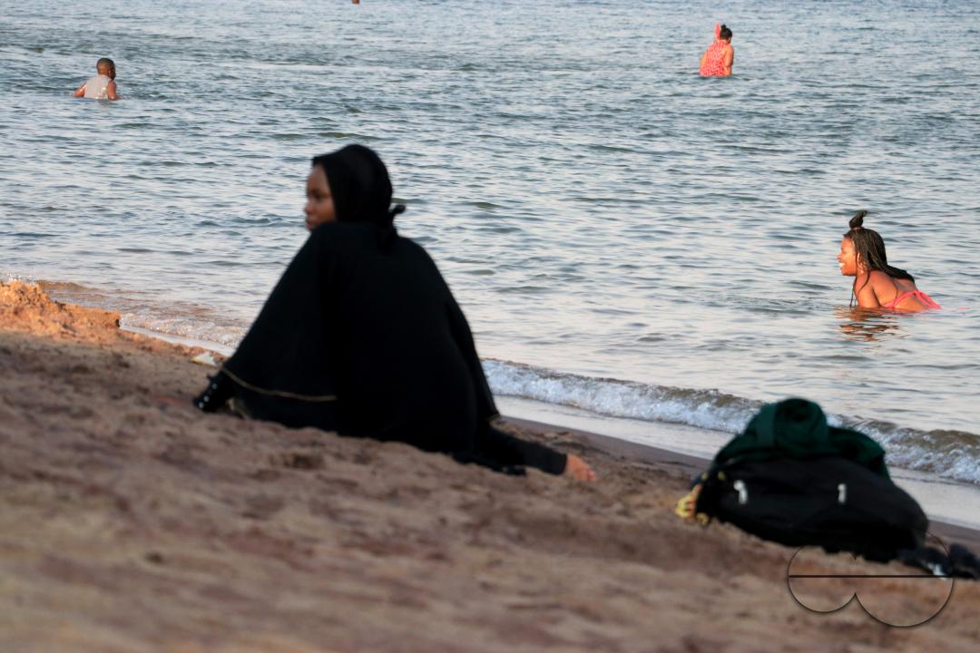 Swimmers are seen in Lake Malawi, while a woman in a hijab is seen sitting on the shores of Lake  Malawi at Senga Bay