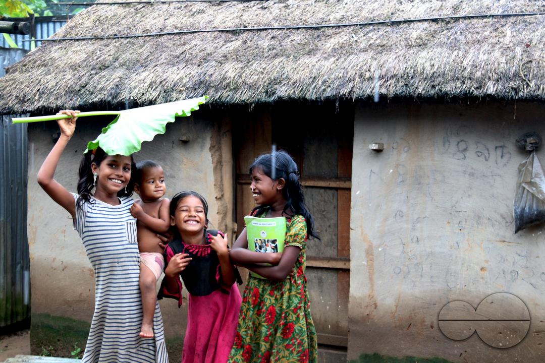 Rural Bangladeshi children happily posing for a photograph while covering their heads with a big leaf to prevent the sun