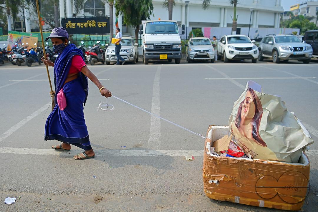 An employee of the municipality pulls a garbage collection box while sweeping and collecting garbage into it in Agartala