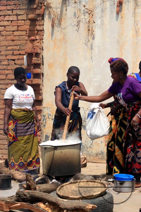 Women help each other to prepare thick porridge known in vernacular as 'nsima.' The women were cooking for a large number of people at a party in Mchinji district, Malawi.