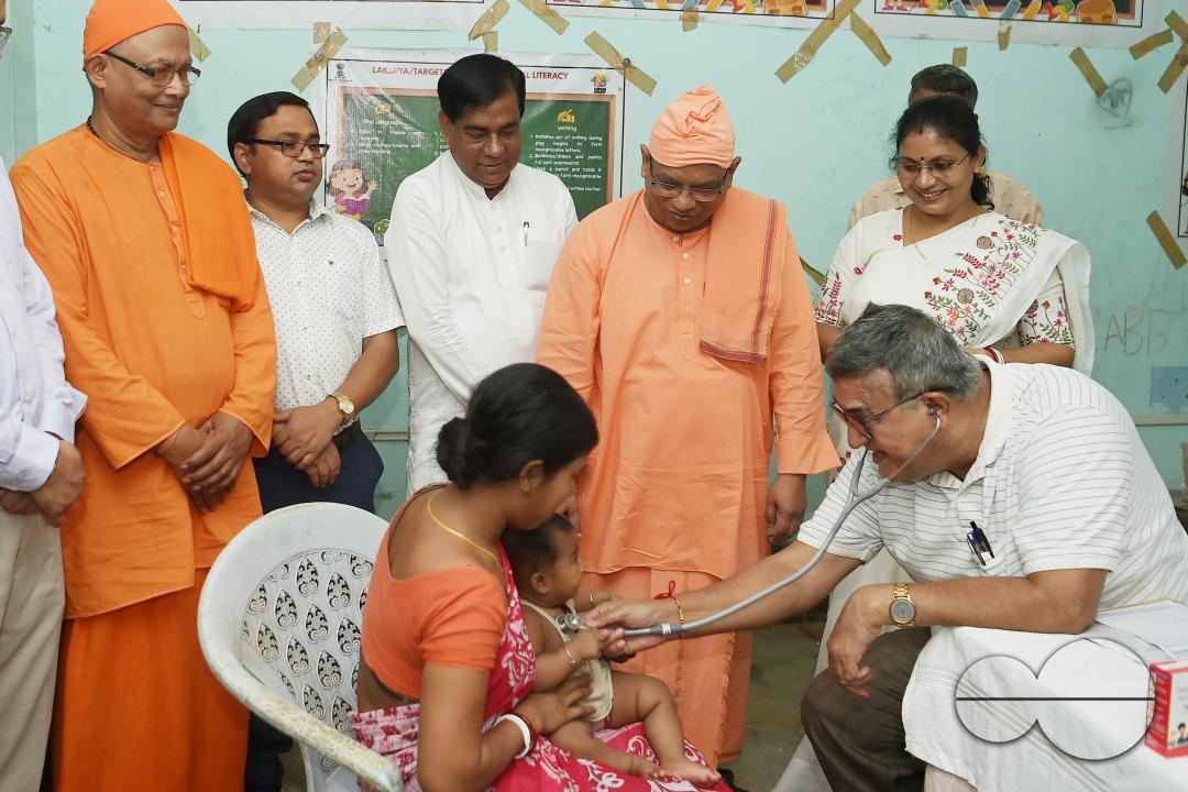 A doctor examining a boy during a visit by Swami Shubhakarananda (Maharaj) - Secretary of Ramakrishna Mission, along with Mayor Deepak Majumdar, the District Magistrate, and other officials inspect a health camp for flood victims at a temporary relief ca