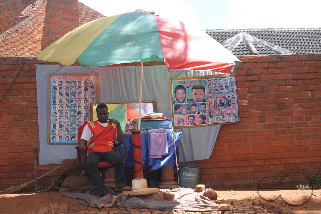 Joshua, a barber is seen outside his workplace, offering barber services on the side of a busy road in Harare