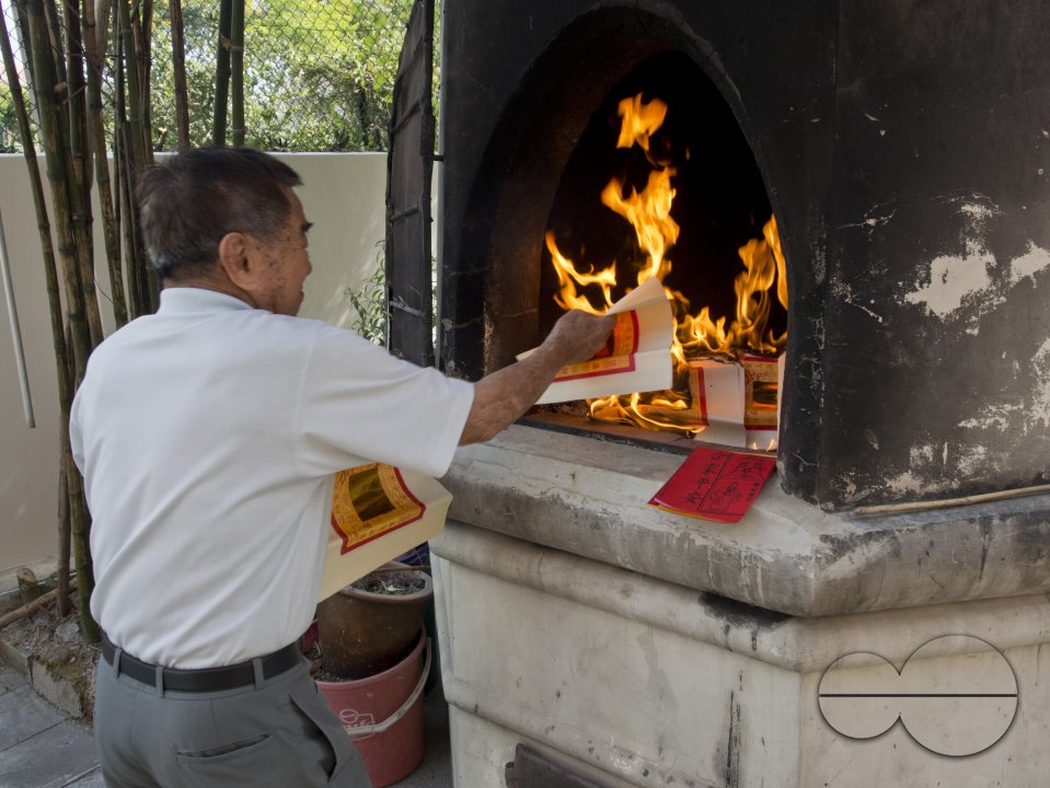 Elderly man burning paper money at a temple on the eve of Chinese New Year in Singapore