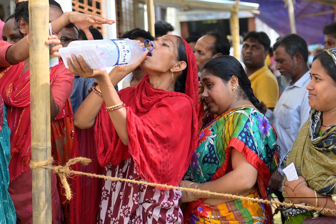 A woman takes a refreshing break while patiently waiting in line to cast her vote for the first phase of Lok Sabha elections in Agartala