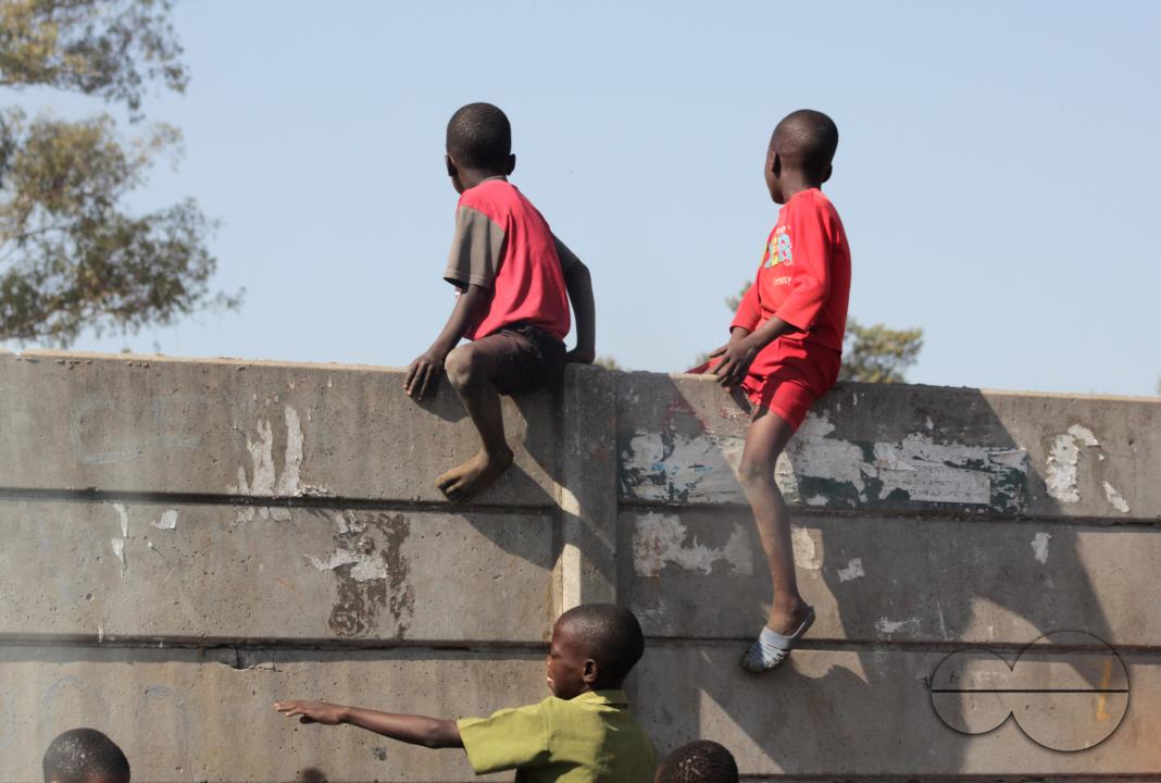 Young boys are sitting on a pre-cast wall to see proceedings that were happening inside the wall in Harare, Zimbabwe.