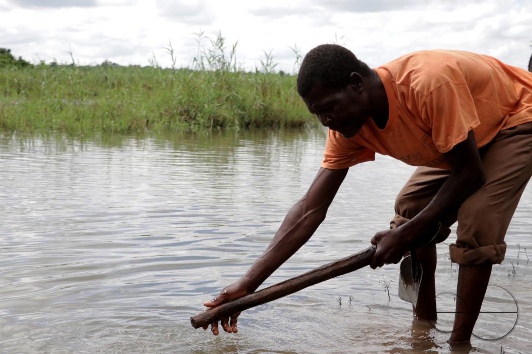 A man is seen cleaning his hoe after planting trees on the banks of the Bua River in Kasungu District