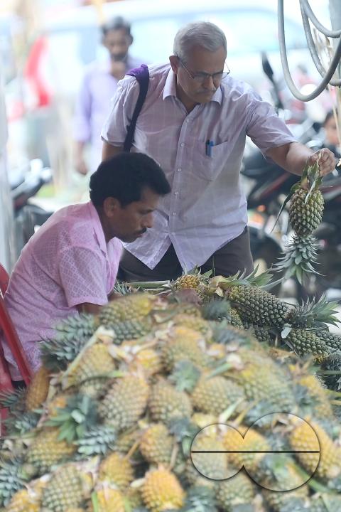 A city dweller purchases pineapple, a renowned summer fruit of Tripura, from a vendor's stall at a bustling roadside fruit market in Agartala