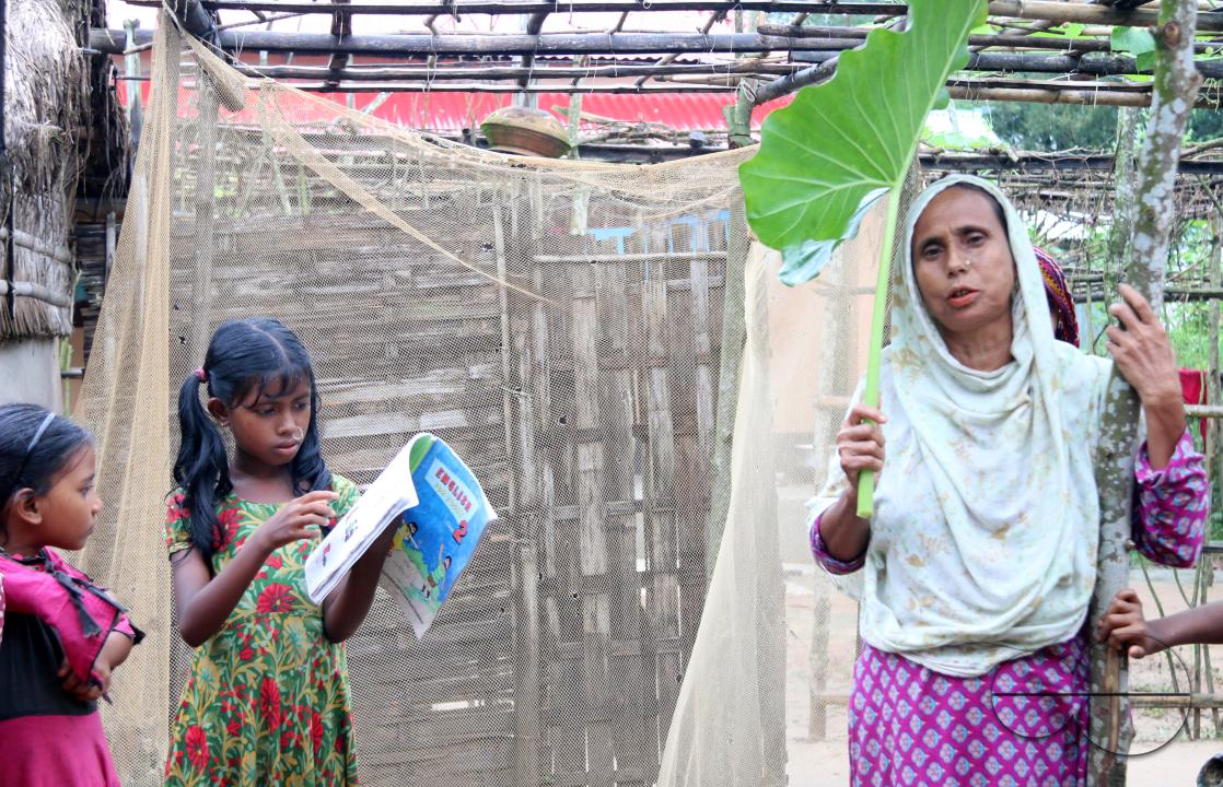 Rural Bangladeshi woman covering her head with a big leaf to prevent the sun
