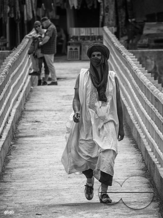 A local arab man in traditional dress crossing a bridge in Merzouga, a small Moroccan town in the Sahara Desert, near the Algerian border