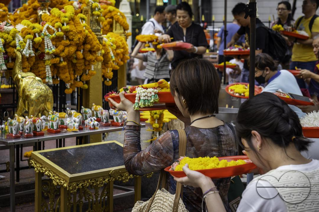 In the heart of downtown Bangkok, an Asian woman engages in prayer with in her hands an offering basket, at the Erawan Shrine