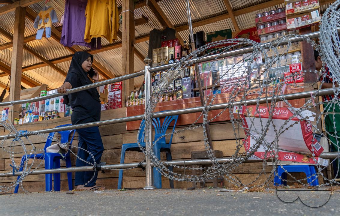 Visitors, traders and illegal Burmese immigrants walk by barbed wire at the Thai side of the Thailand - Myanmar border at Mae Sot, Thailand.