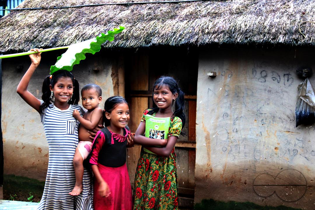 Rural Bangladeshi children happily posing for a photograph while covering their heads with a big leaf to prevent the sun