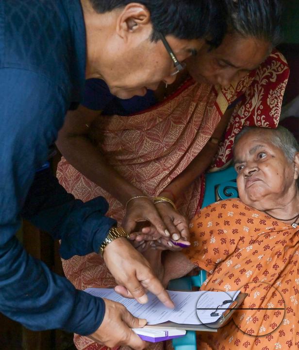 An old lady aged 104, going through the pre vote procedures before casting her postal ballot vote with the assistance of her family members at her house in front of the team of election officials and security personnel in Agartala