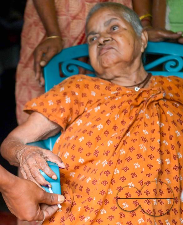 An election official marking the finger an old lady aged 104, before casting her postal ballot vote with the assistance of her family members at her house in front of the team of election officials and security personnel in Agartala