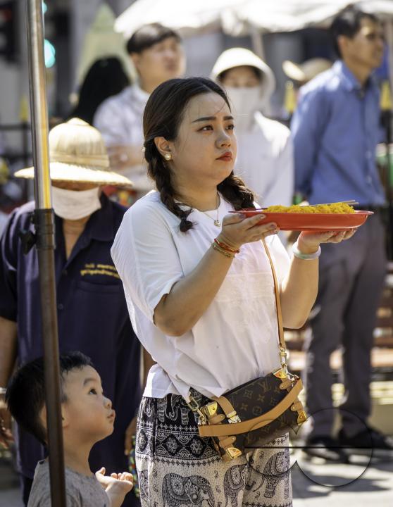 A young Asian woman, accompanied by her son, offers prayers with a basket of offerings, at the Erawan Shrine in downtown Bangkok