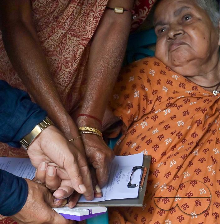 An old lady aged 104, going through the pre vote procedures before casting her postal ballot vote with the assistance of her family members at her house in front of the team of election officials and security personnel in Agartala