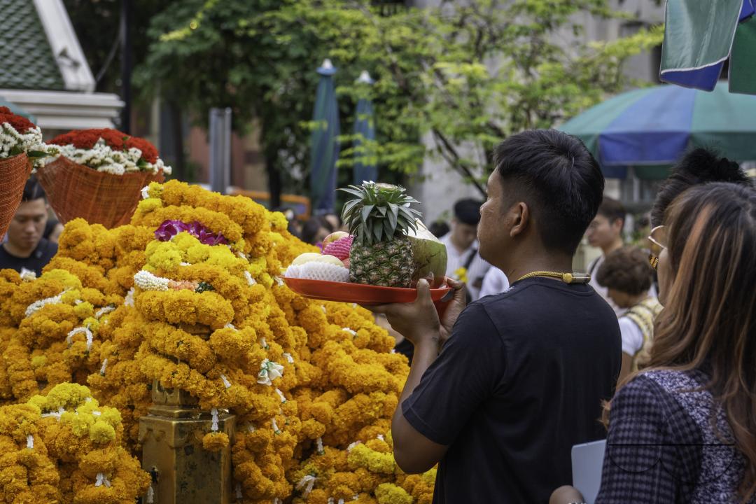 In the heart of downtown Bangkok, at the Erawan Shrine, an Asian man offers his prayers handing a basket filled with fruits purchased as an offering