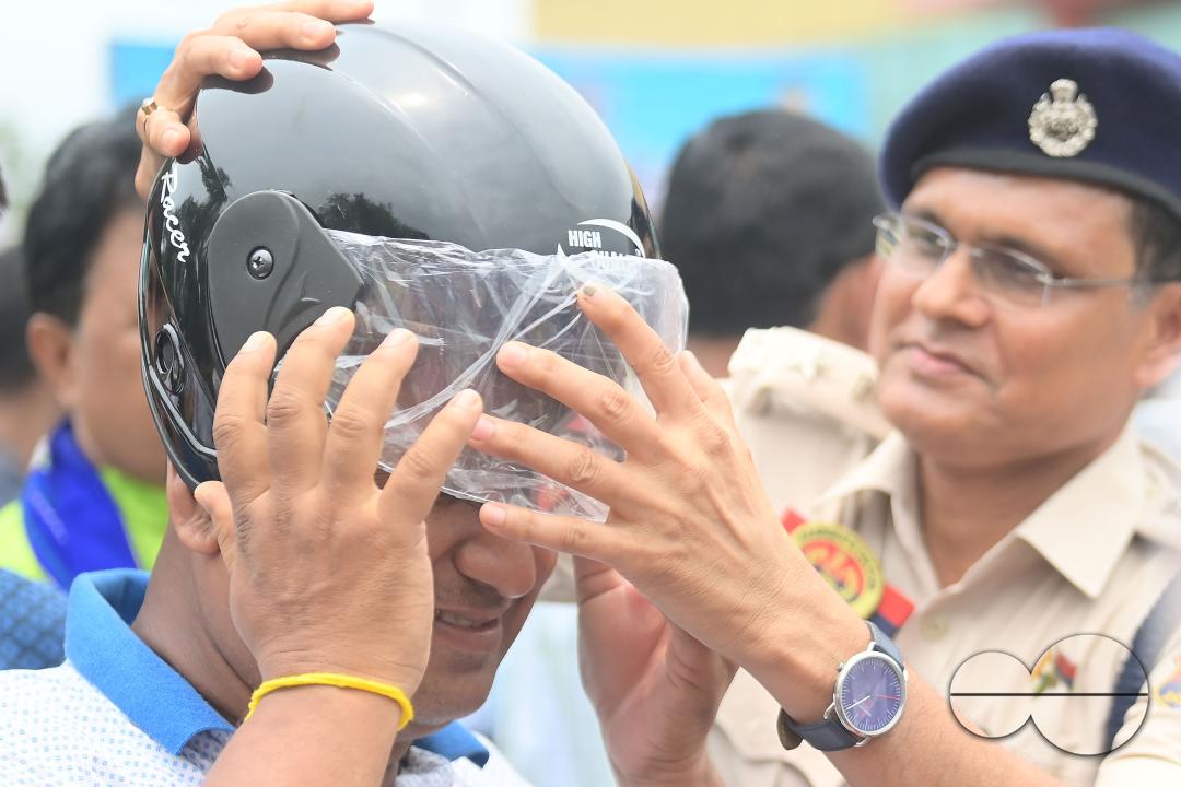 A traffic official puts a helmet on a motorist during a helmet distribution program and a road safety awareness campaign organised by the Tripura Transport Department at Agartala