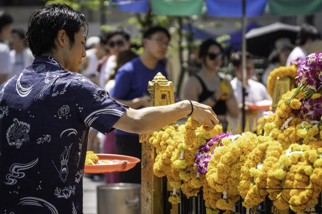 In the heart of bustling downtown Bangkok, an Asian man places a flower garland as an offering at the revered Erawan Shrine, honoring tradition