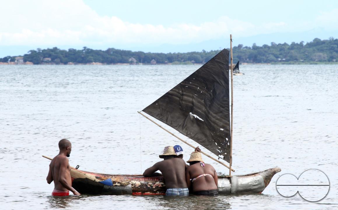 People gather around a canoe to buy fresh fish caught in Lake Malawi, Senga Bay