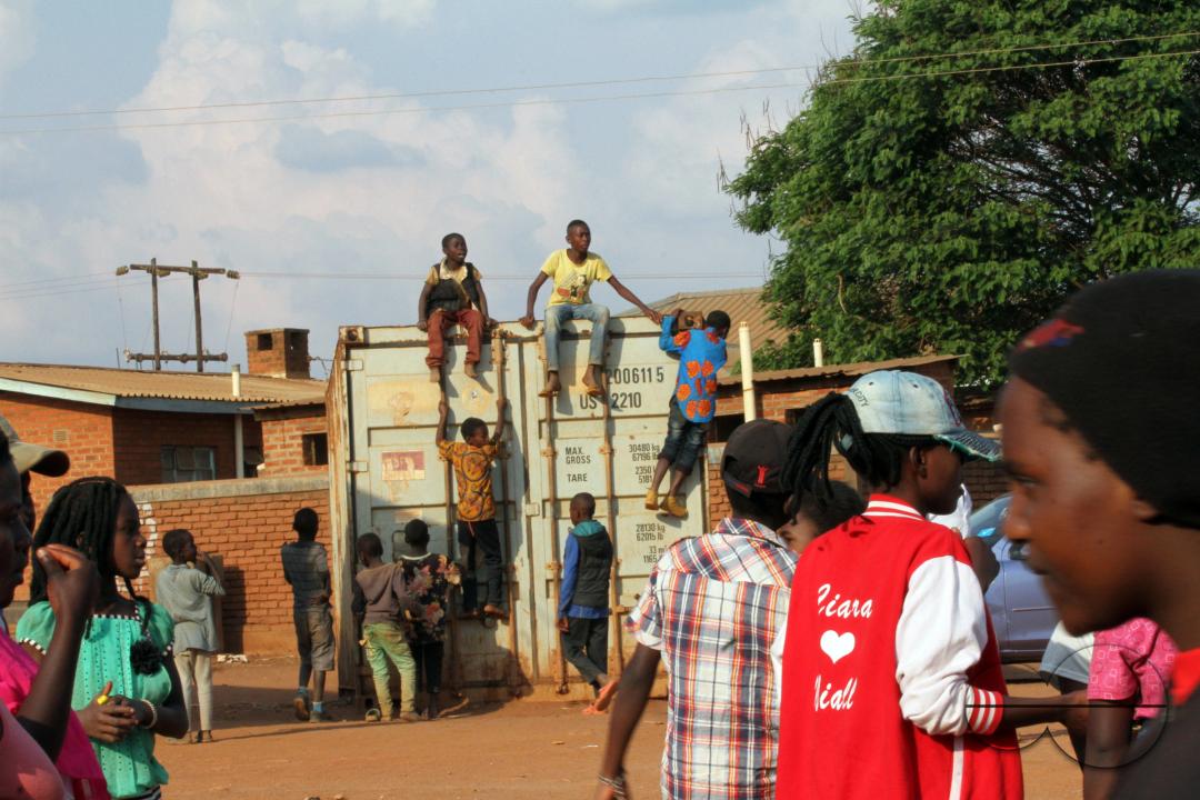 Young people are seated on a container, while others attempt to climb up to see the activities taking place during a festival at Dzaleka Refugee Camp, in Dowa District, Malawi.