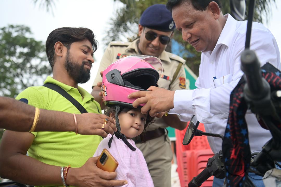 A traffic official puts a helmet on a kid who is riding on a motorcycle with her father during a helmet distribution program and a road safety awareness campaign organised by the Tripura Transport Department at Agartala