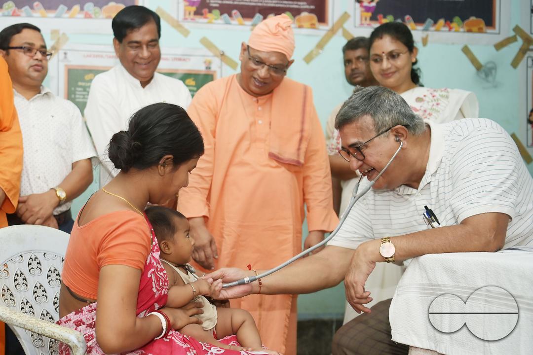 A doctor examining a boy during a visit by Swami Shubhakarananda (Maharaj) - Secretary of Ramakrishna Mission, along with Mayor Deepak Majumdar, the District Magistrate, and other officials inspect a health camp for flood victims at a temporary relief ca