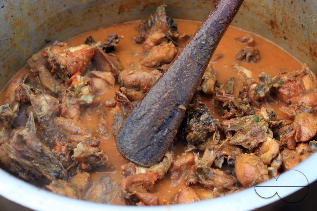 A pot of chicken stew is seen on an open fire